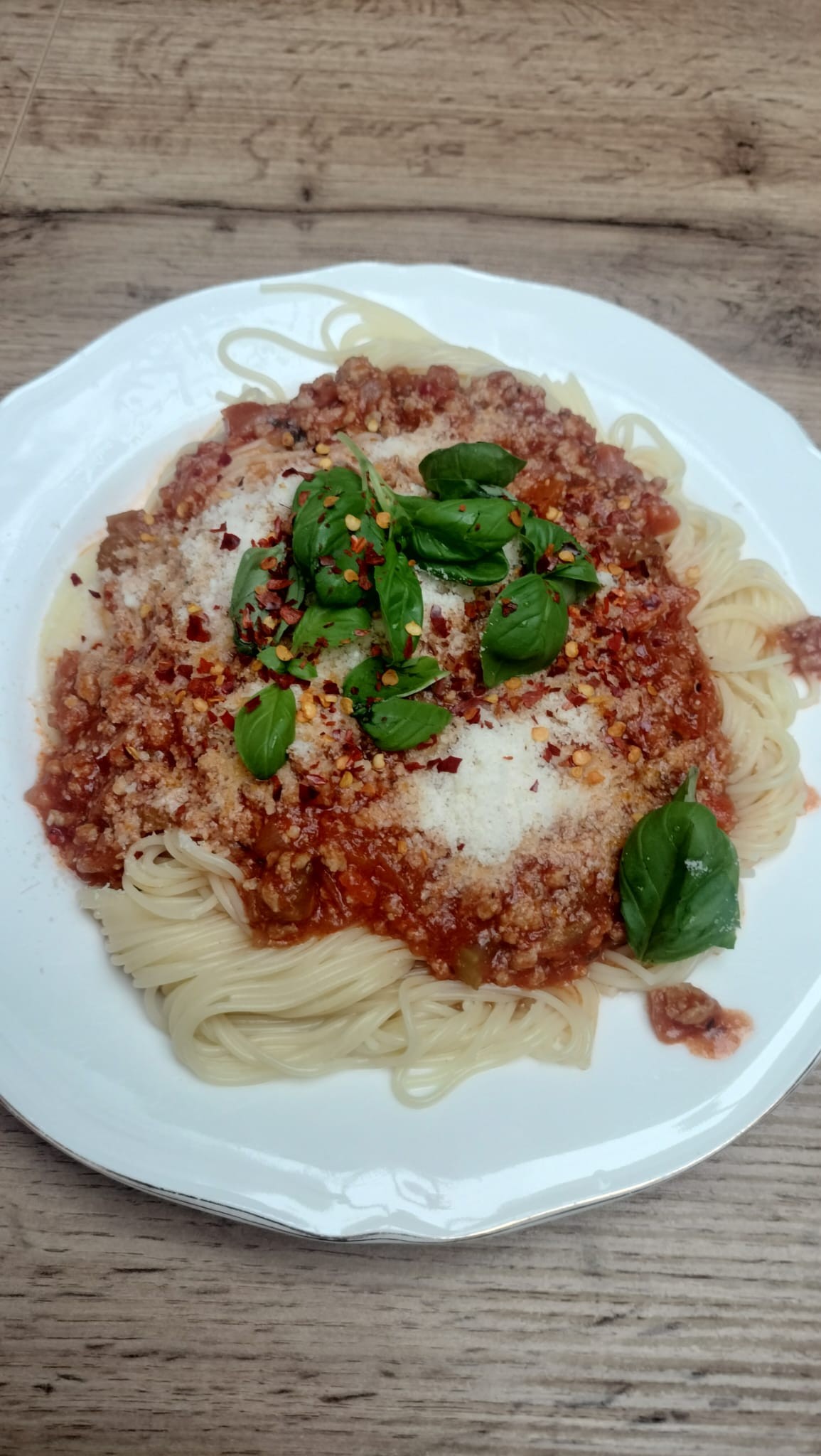 Biały talerz z makaronem, sosem pomidorowym i liśćmi bazylii.  