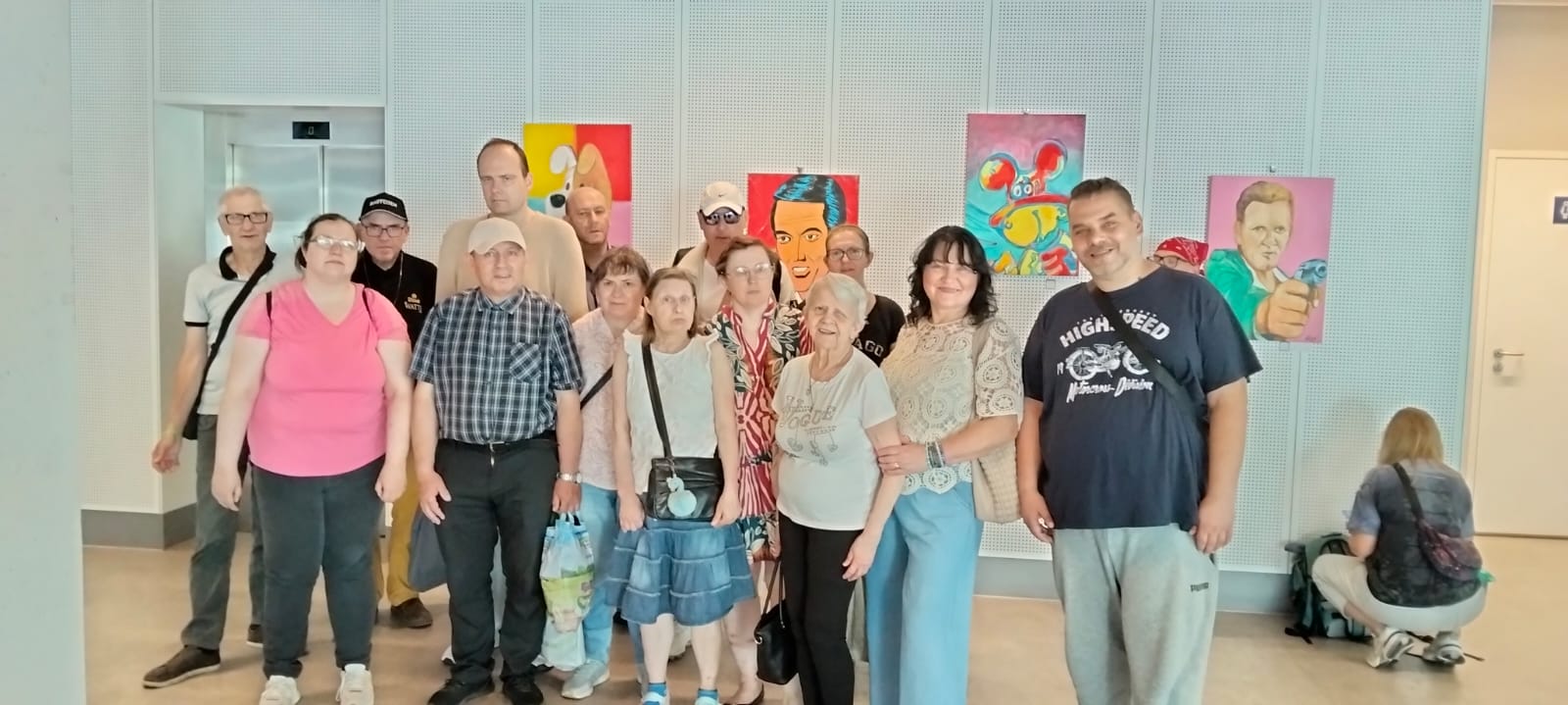 Grupa osób pozująca do zdjęcia na tle ściany z kolorowymi obrazami.