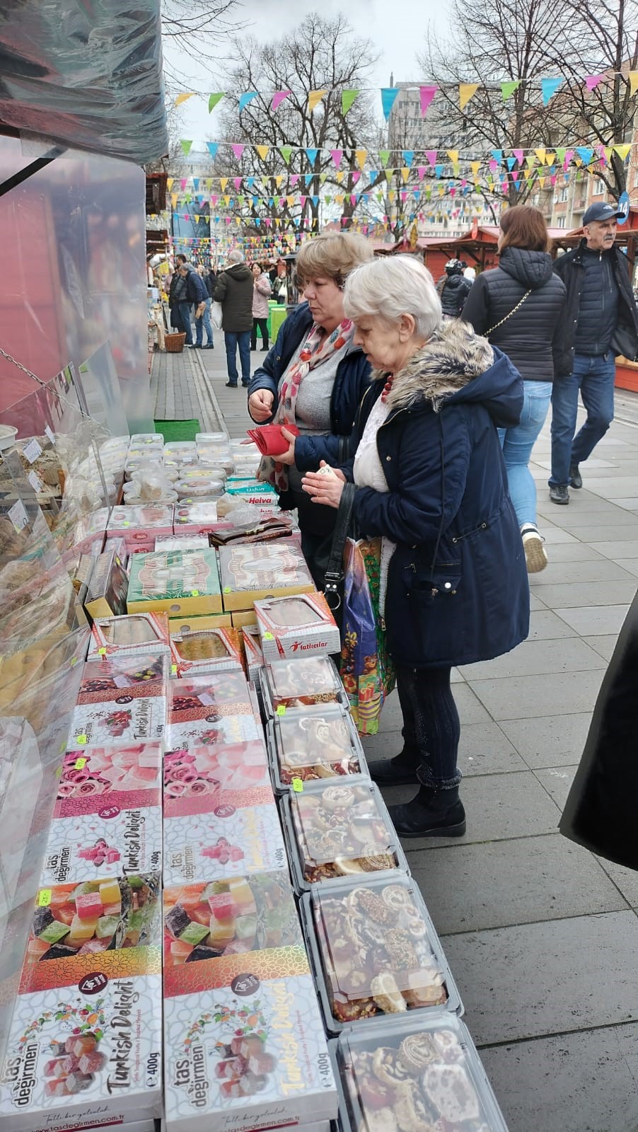 Na pierwszym planie dwie kobiety przy stoisku handlowych ze słodyczami.