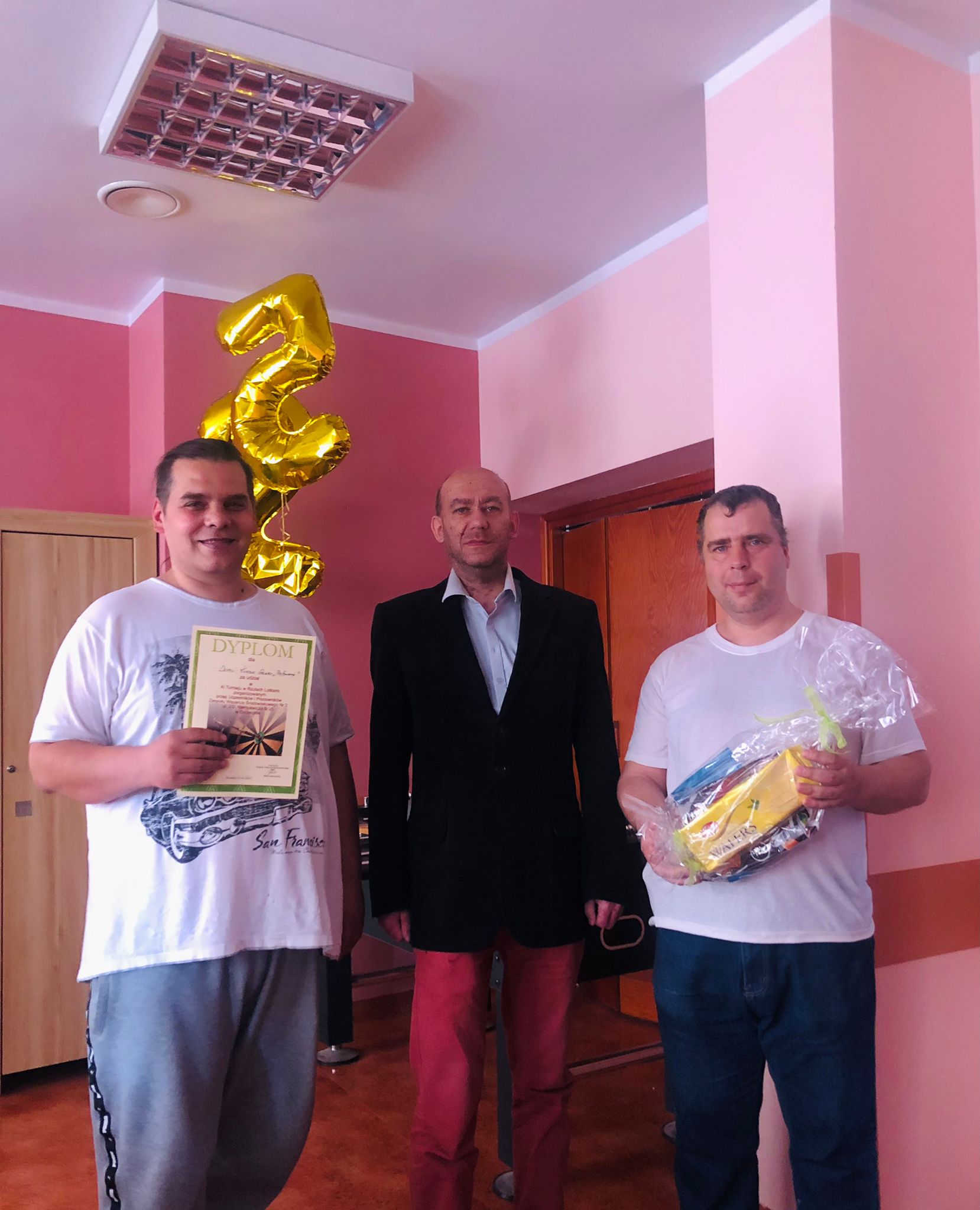Trzech mężczyzn pozujących do zdjęcia z dyplomem i nagrodą rzeczową. 