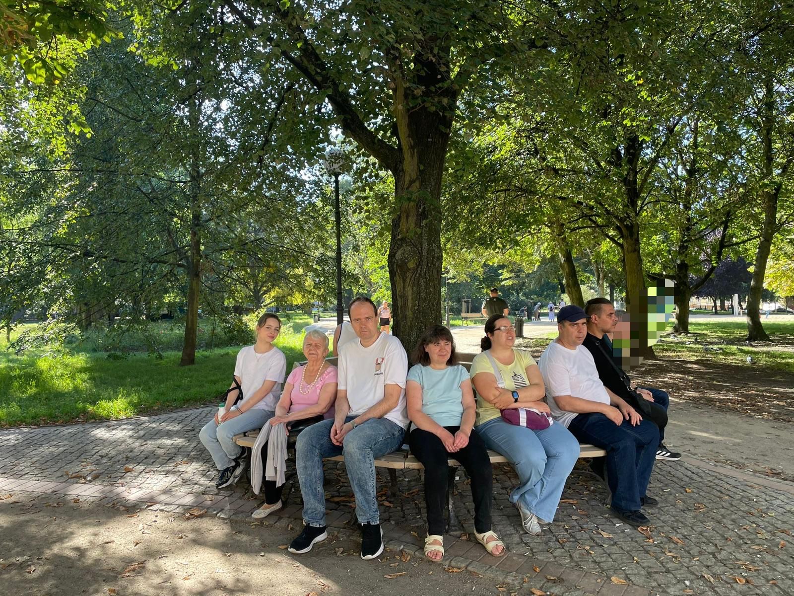 Grupa osób siedzi pod drzewem.
