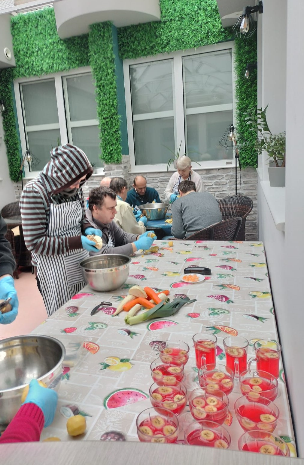 Grupa osób podczas obierania warzyw i przygotowywania deserów. 