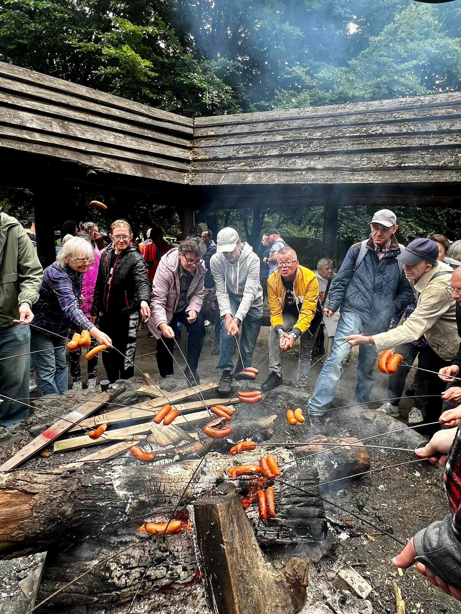 Grupa osób smażąca kiełbaski nad ogniskiem