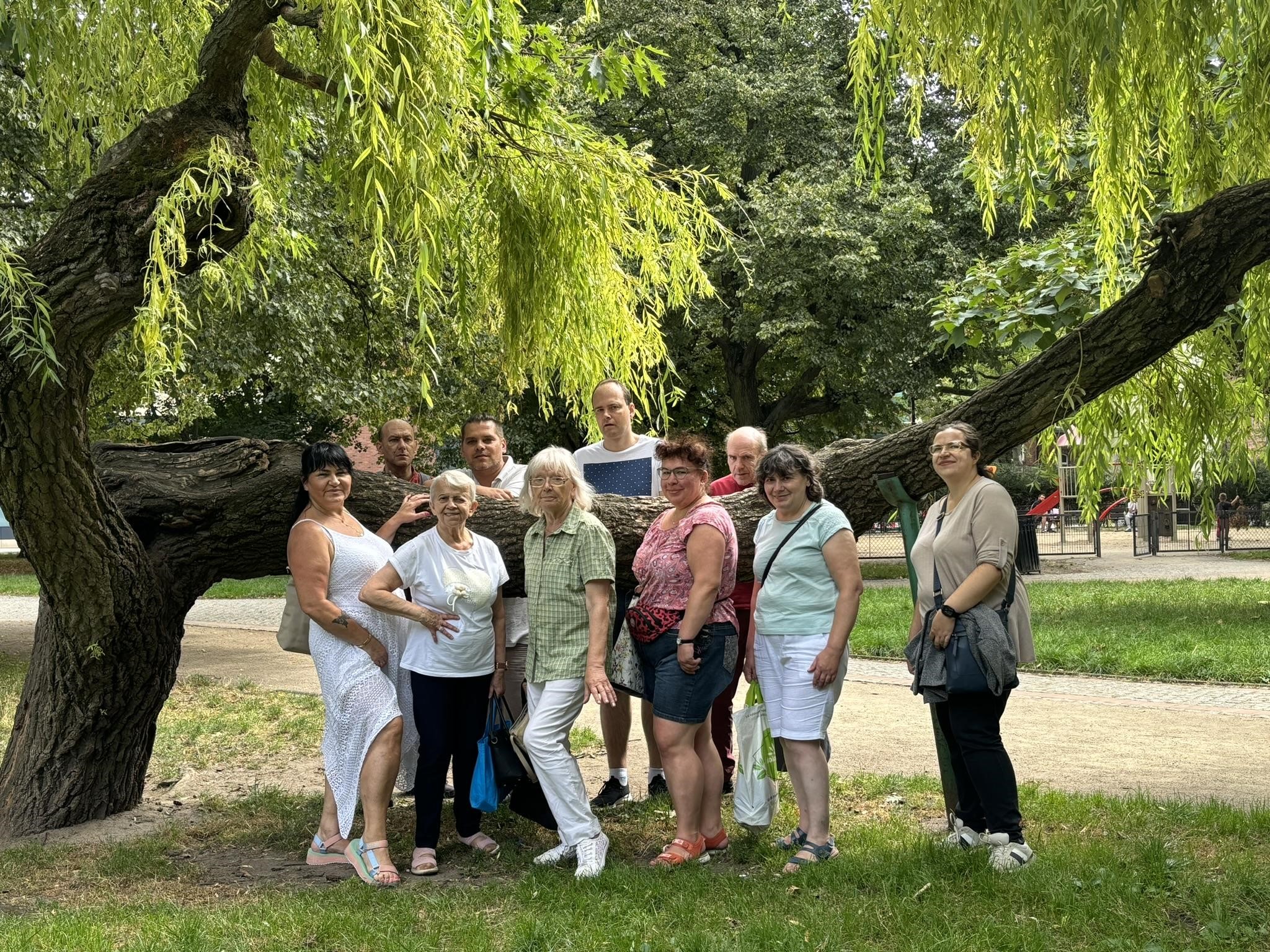 Grupa osób pozująca przy drzewie. W tle zieleń parku.