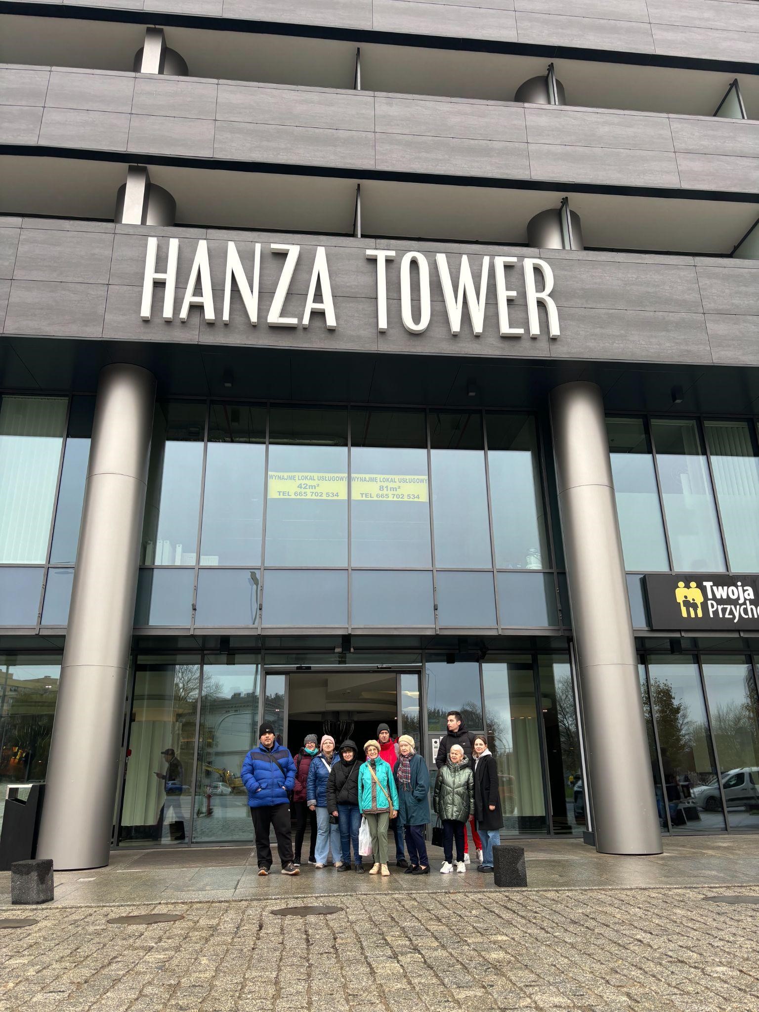 Grupa osób na tle nowoczesnej fasady budynku. Na budynku widać napis – HANZA TOWER