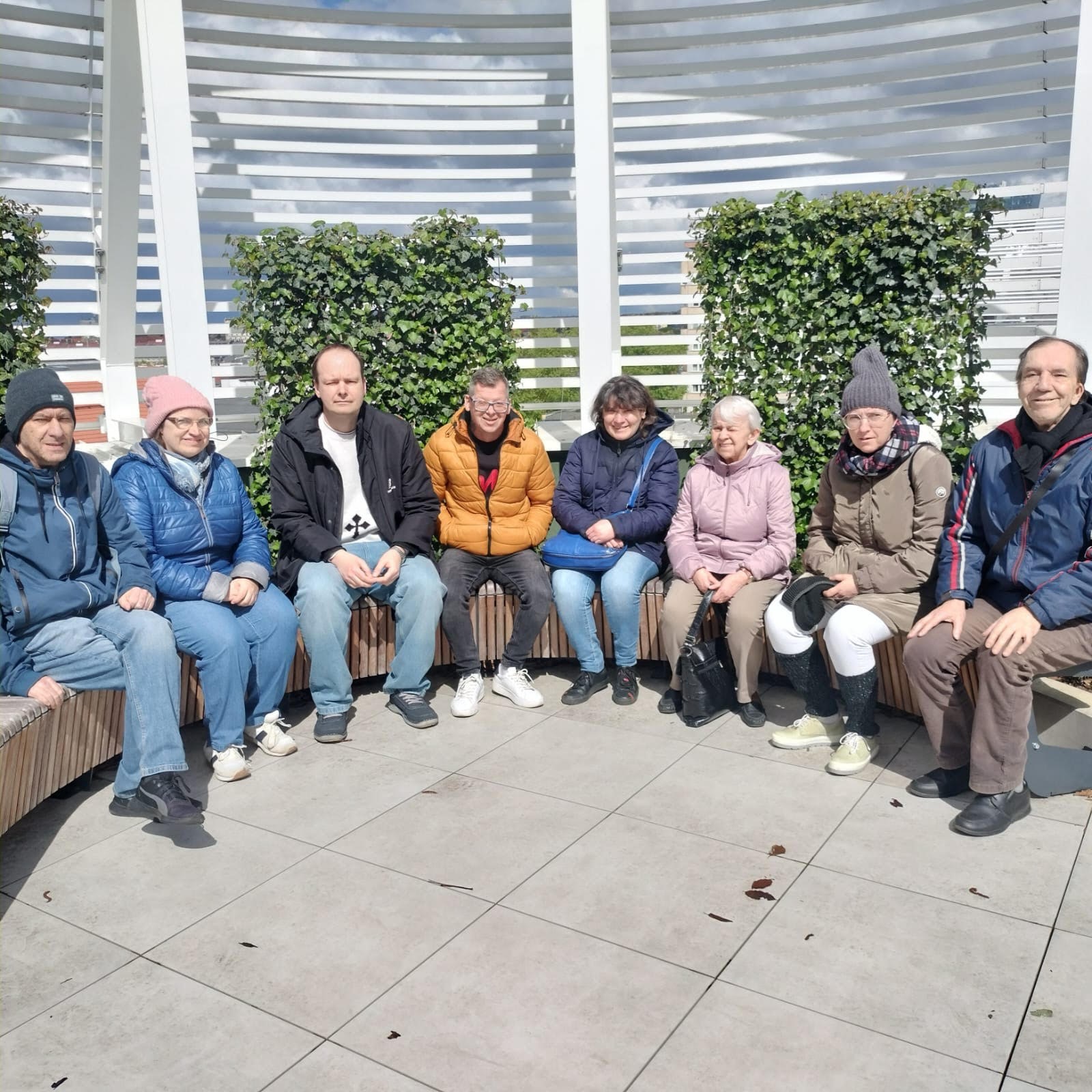 Grupa osób pozująca na ławce W tle zielona roślinność. 