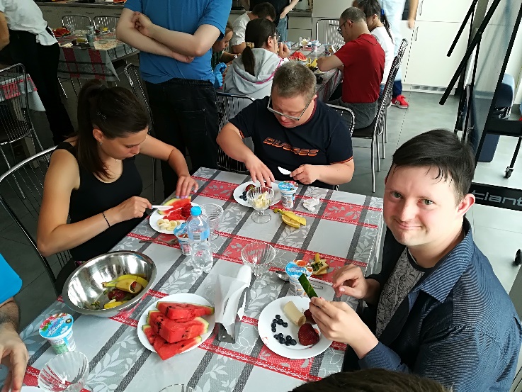 Kobiety i mężczyźni siedzą przy stole i kroją owoce