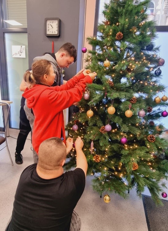 Kobiety i Mężczyźni wieszający kolorowe bombki na choince.