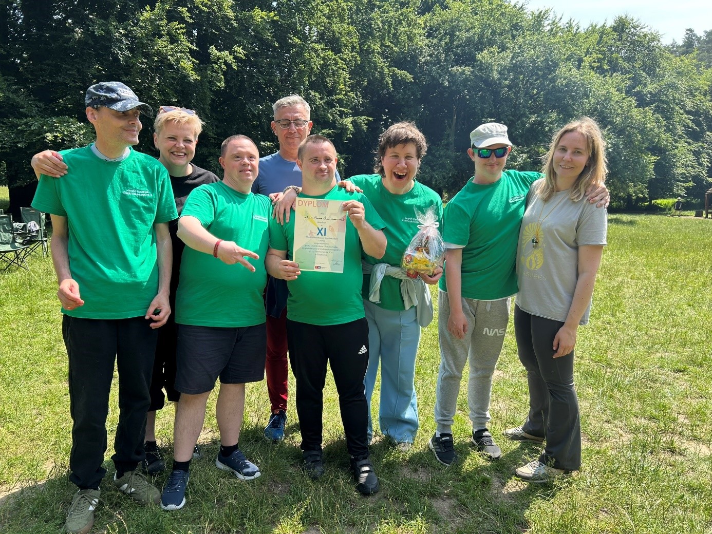 Grupa kobiet i mężczyzn pozuje do zdjęcia. W tle drzewa. 