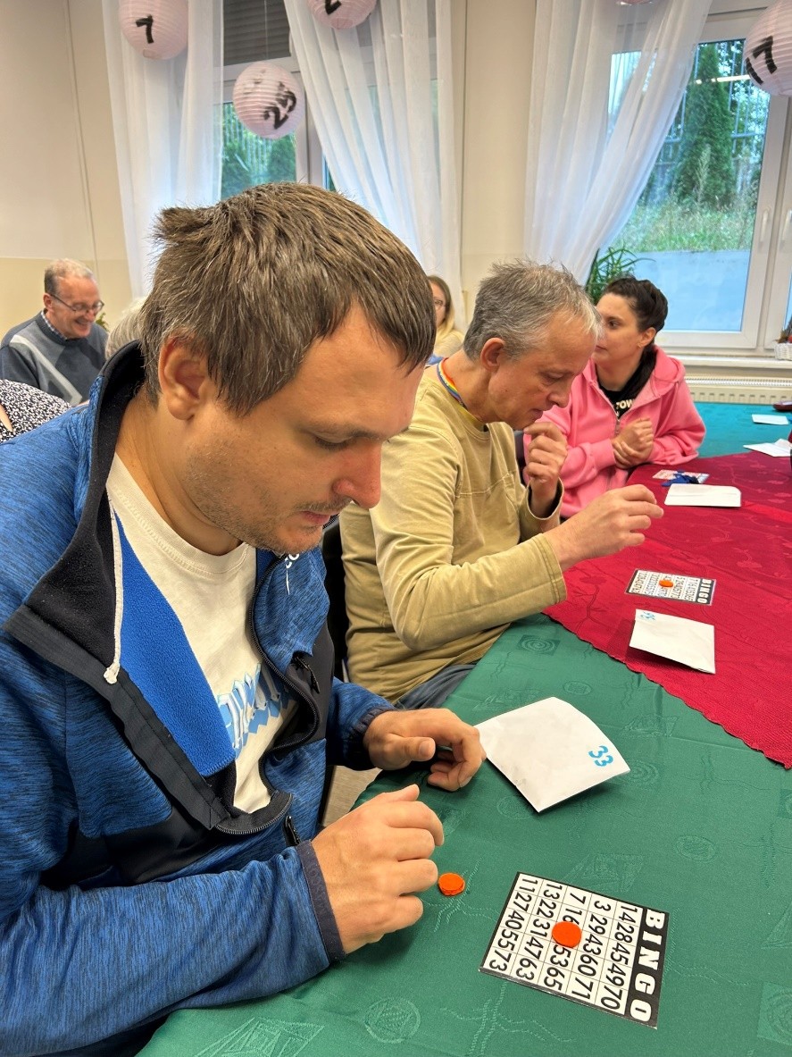 Dwóch mężczyzn i jedna kobieta podczas gry. Na stole leżą karty do grania. 