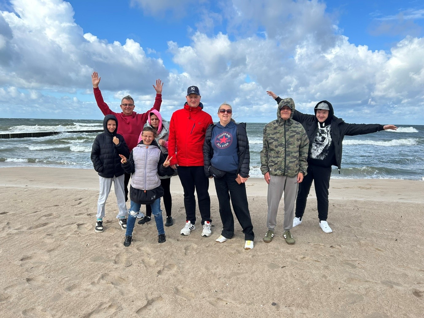 Trzy kobiety i pięciu mężczyzn stoi na piasku na tle morza. 