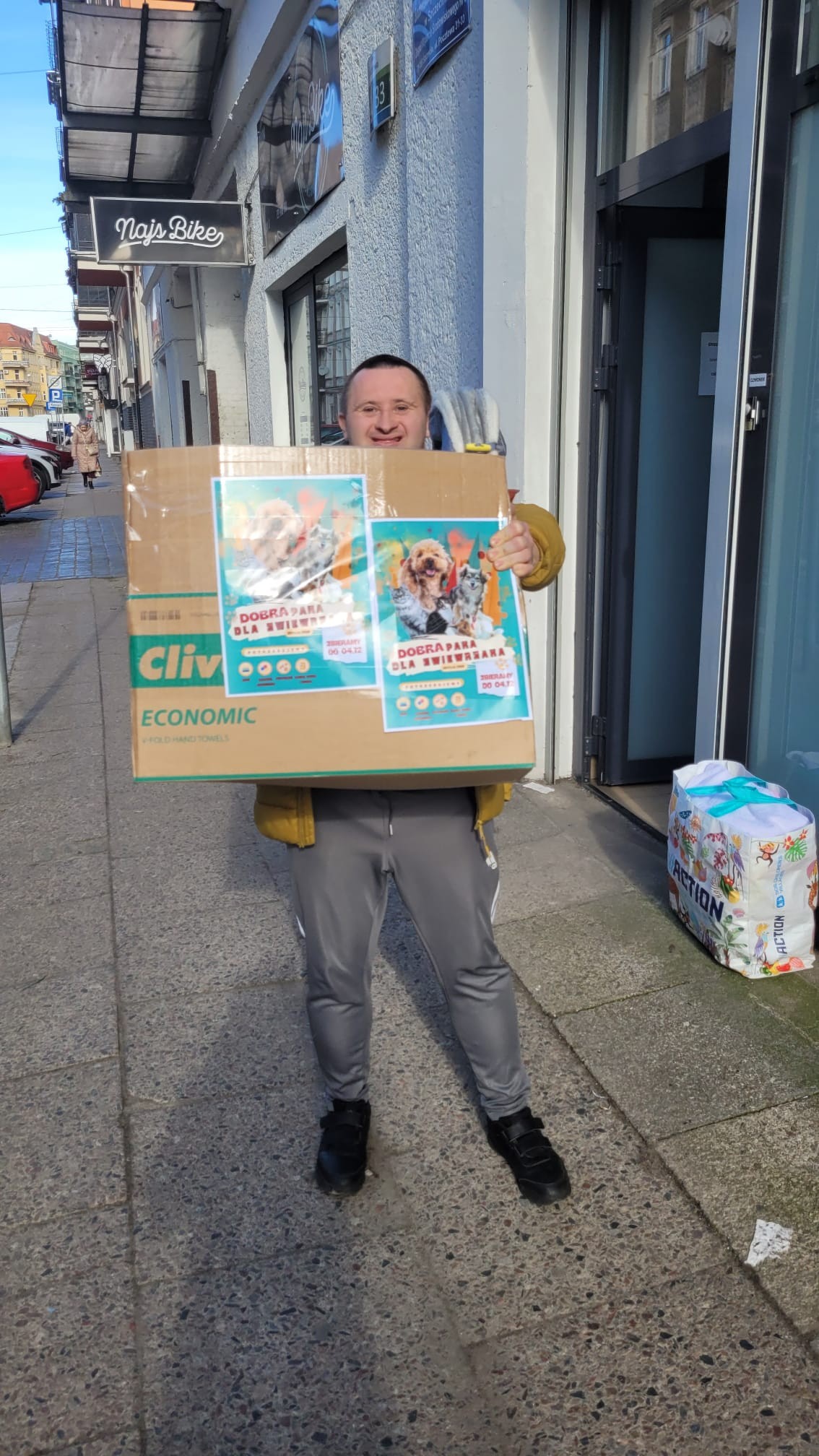 Na zdjęciu uśmiechnięty mężczyzna trzyma dużą paczkę. 