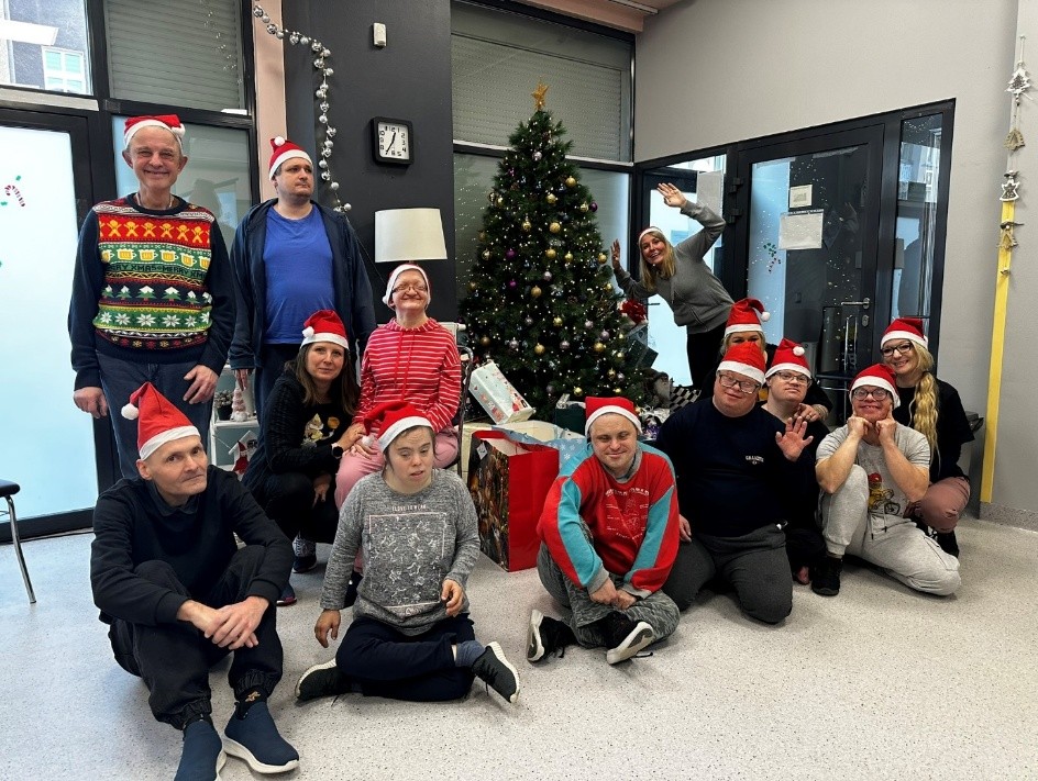 Grupa kobiet i mężczyzn pozuje do zdjęcia. W tle choinka i prezenty. 