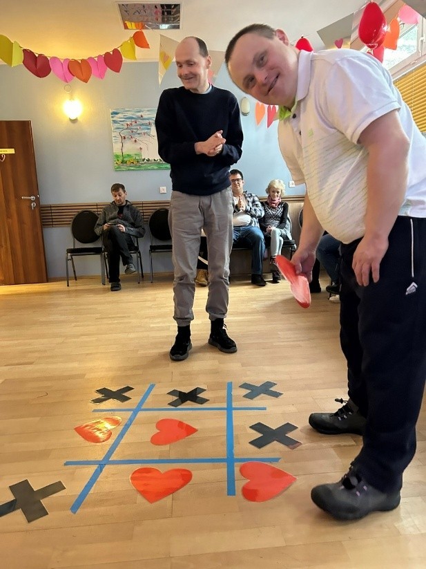 Dwóch mężczyzn gra w grę. Gra rozłożona jest na podłodze. 